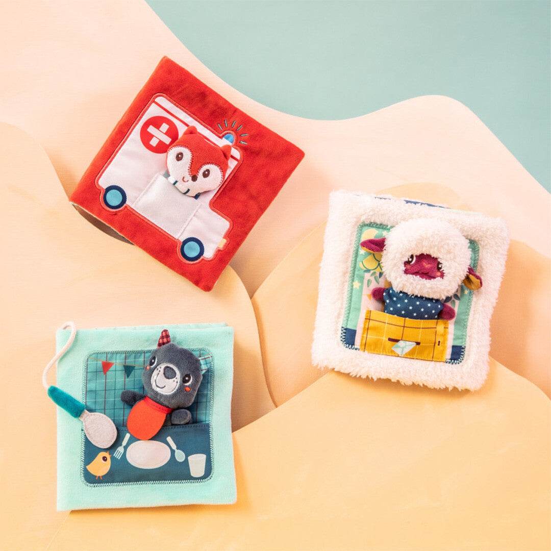 Drie Lilliputiens activiteitenboeken voor baby's, waaronder de rode met ambulance en vos, op een golvende achtergrond.