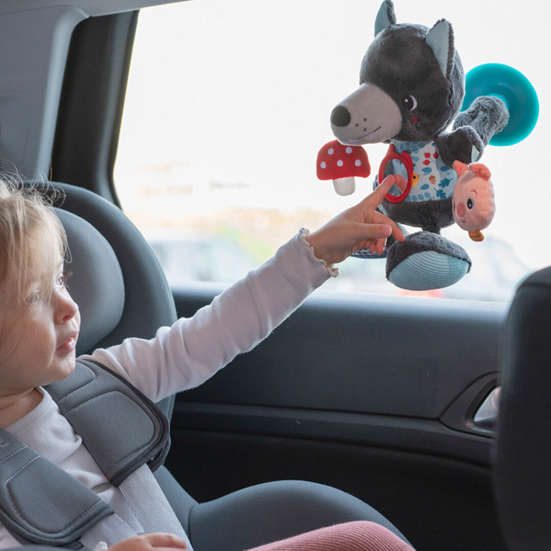 Een kind in een autostoel raakt de Lilliputiens activiteitenknuffel Louis de wolf aan, die met een zuignap aan het raam hangt.