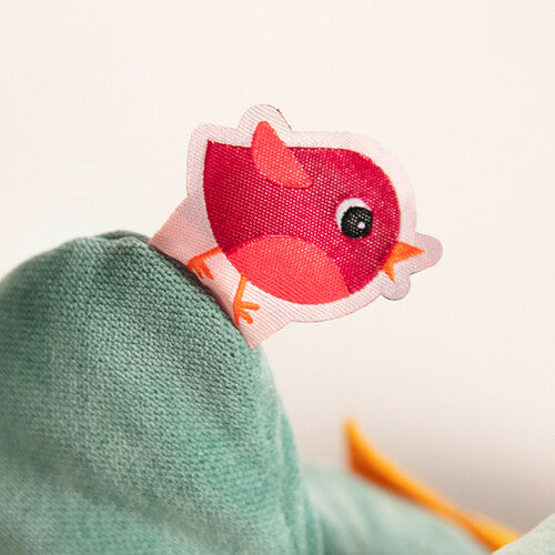 Close-up van een rood vogeltje met een roze snavel, bevestigd aan de groene Lilliputiens activiteitenknuffel.