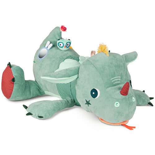 Lilliputiens groene activiteitenknuffel in de vorm van een draak of dinosaurus, liggend op de grond.
