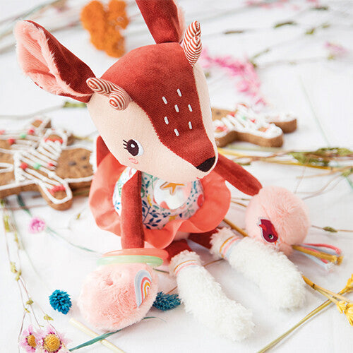 Lilliputiens activiteitenknuffel Stella, een bruin hertje, zittend tussen gedroogde bloemen en koekjes.