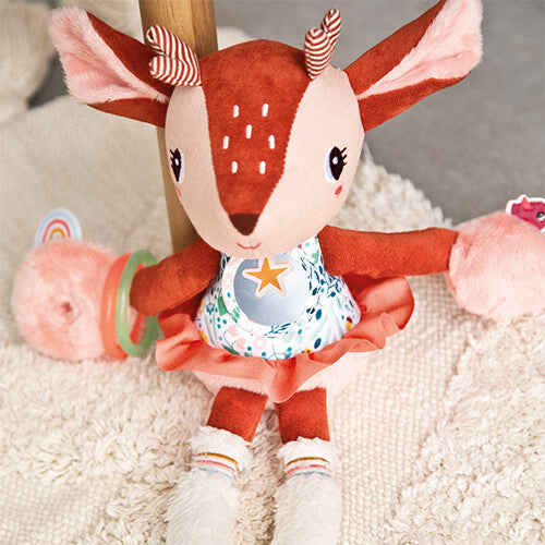 Lilliputiens activiteitenknuffel Stella, een bruin hertje met bloemenjurk en rammelaars, zittend op een wit kleed.