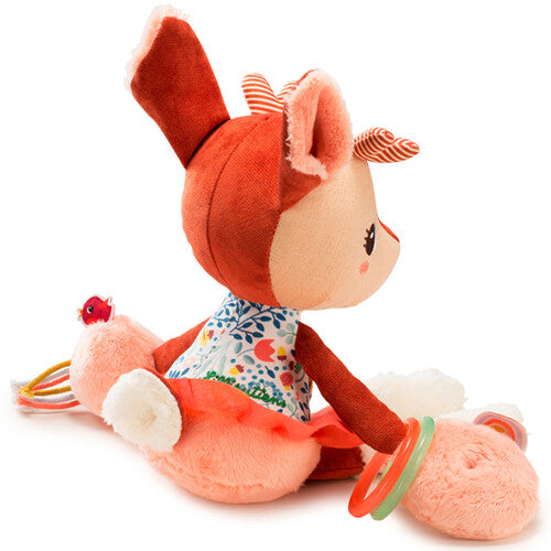 Lilliputiens activiteitenknuffel Stella, een bruin hertje met bloemenjurk en rammelaars, zittend vanuit een schuine hoek.
