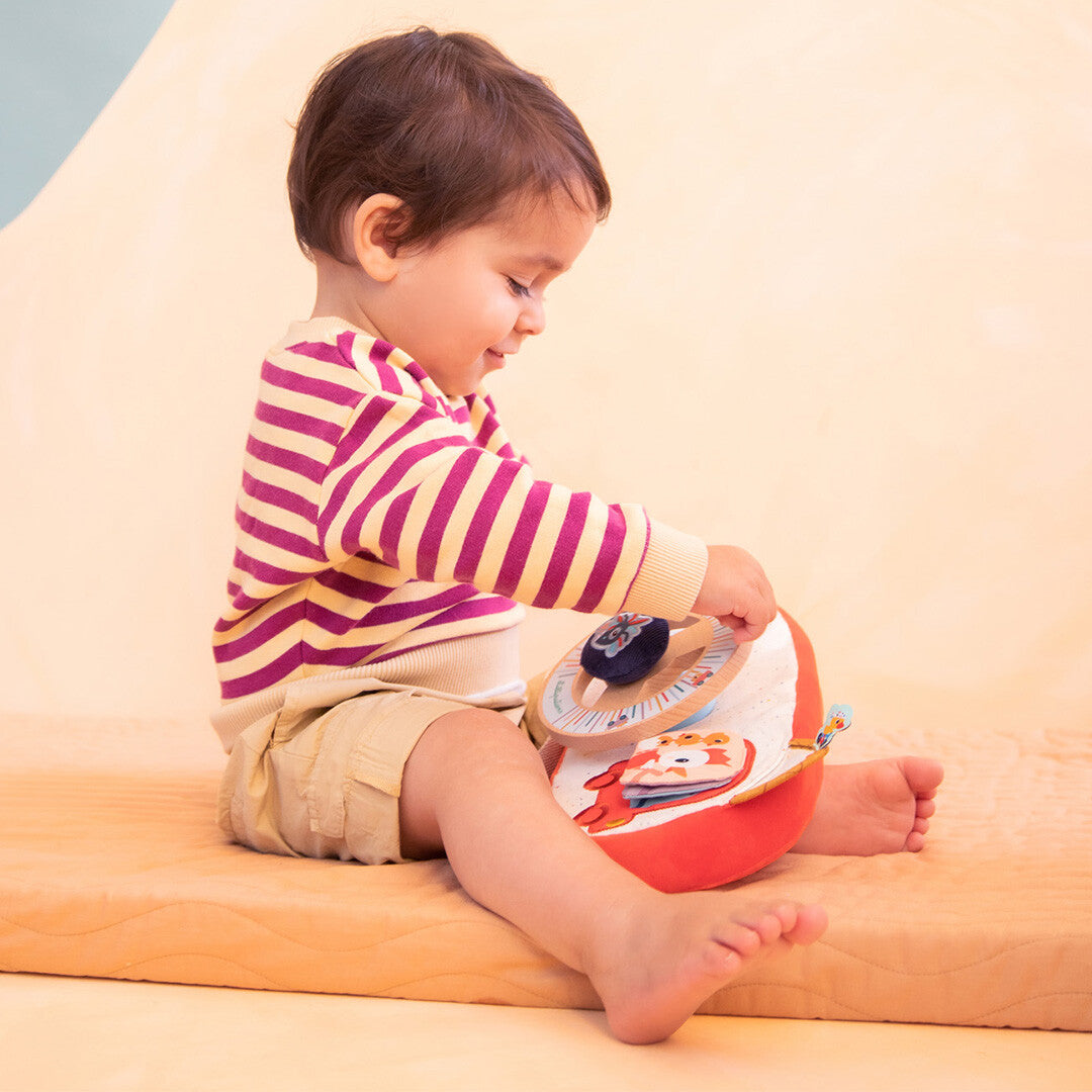 Een baby speelt zittend op een mat met het Lilliputiens activiteitenpaneel auto - boerderij.