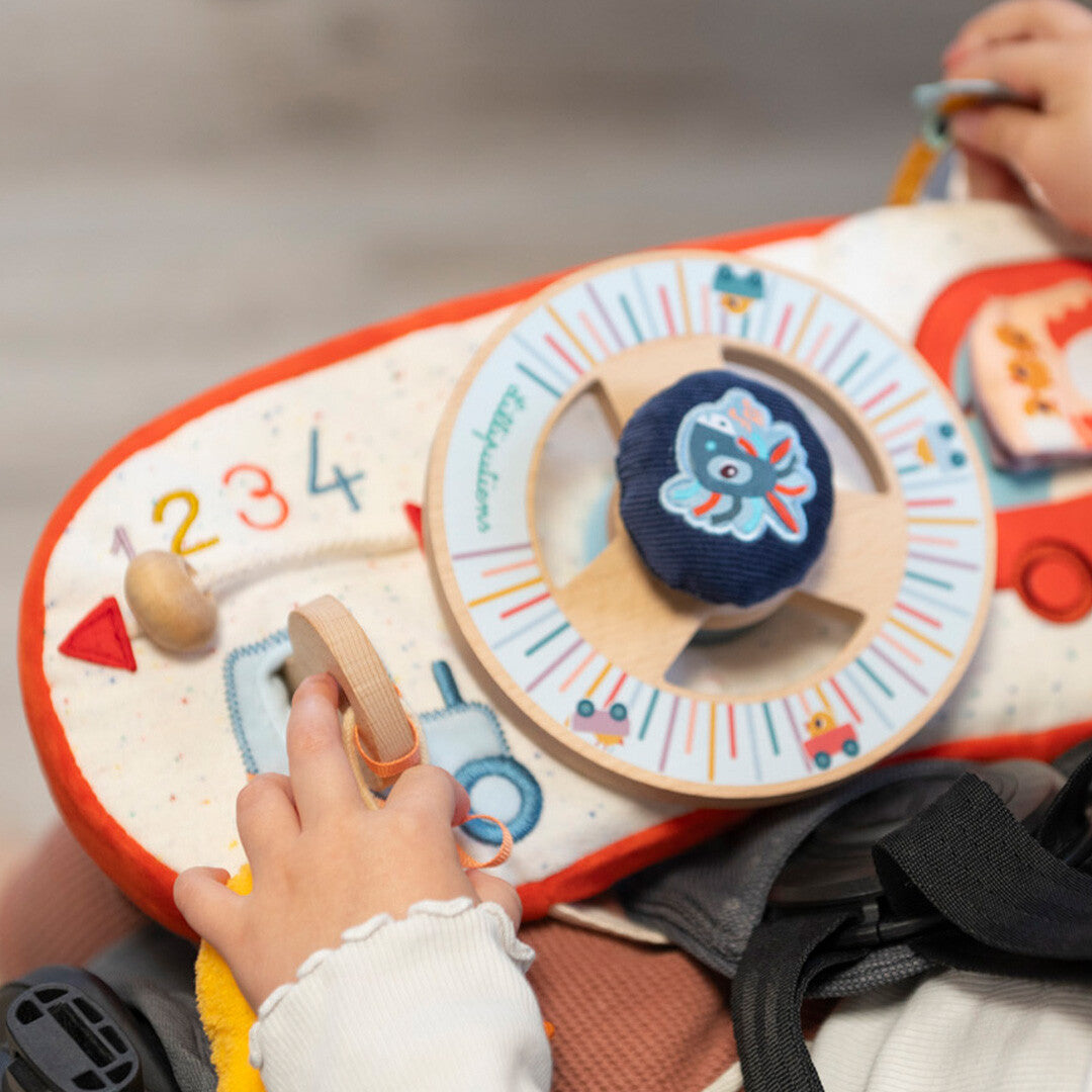 Een kinderhand speelt met het Lilliputiens activiteitenpaneel auto - boerderij, bevestigd aan een kinderwagen of autostoel.