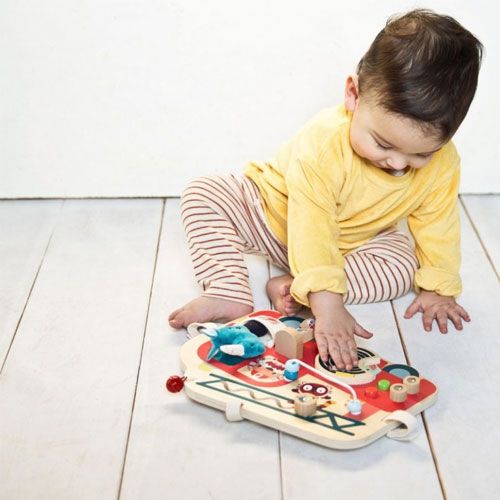 Een baby speelt op de vloer met het lilliputiens houten activiteitenpaneel brandweerwagen.