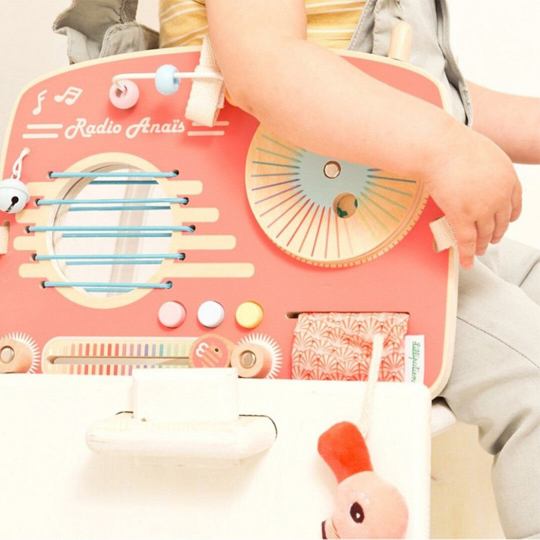 Een close-up van een babyhandje dat het Lilliputiens activiteitenpaneel in de vorm van een roze radio aanraakt.