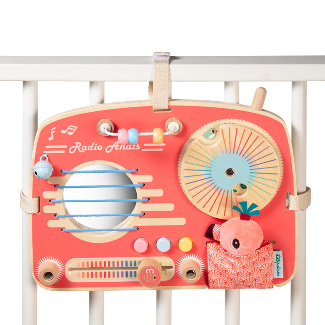 Lilliputiens activiteitenpaneel in de vorm van een roze radio hangt aan een wit babybedje.