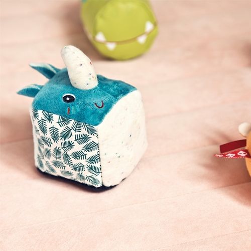 Lilliputiens neushoorn rammelaar met blauw pluche en een wit hoorntje, liggend op een roze ondergrond.