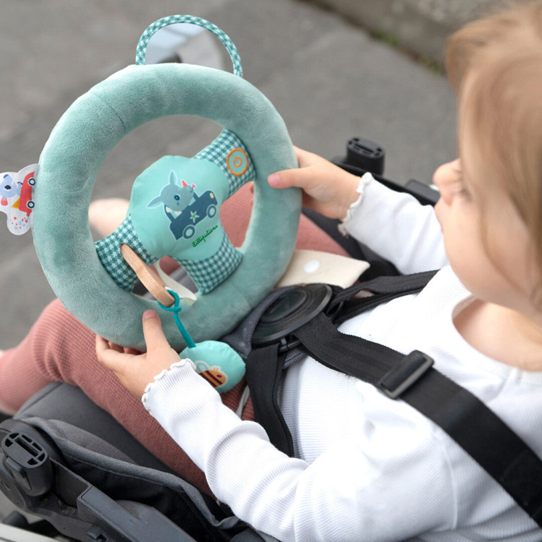 Een baby in een kinderwagen speelt met het Lilliputiens groene pluche activiteitenspeelgoed stuur.