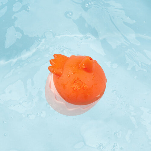 Het Lilliputiens badspeeltje, een oranje kuiken in een roze eierschaal, drijft in het water.