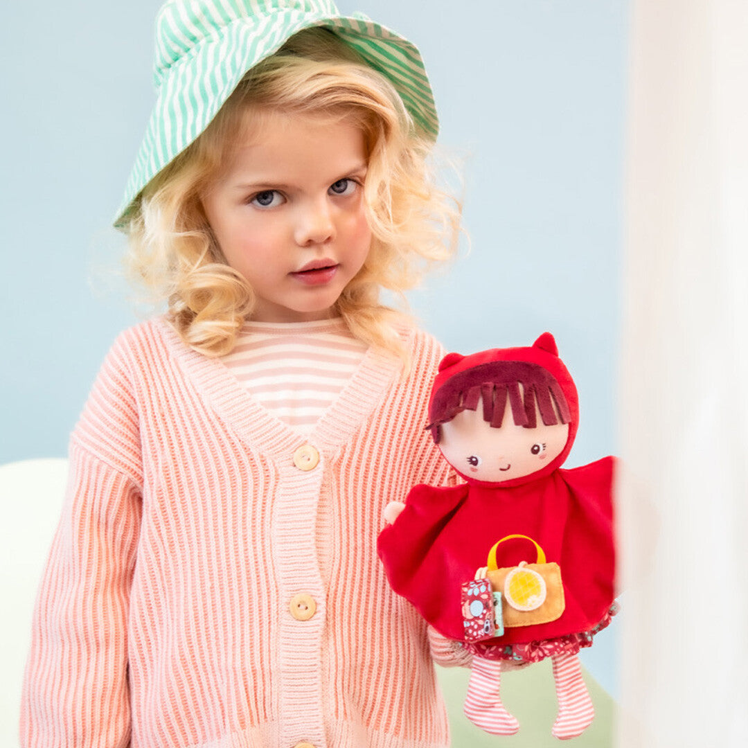 Een meisje met een gestreepte hoed houdt de Lilliputiens handpop Roodkapje vast.
