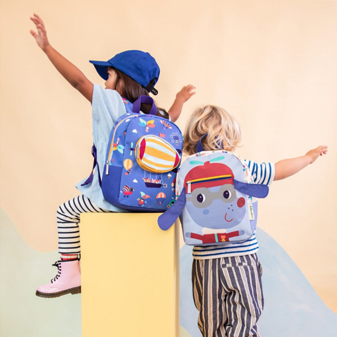 Twee kinderen met Lilliputiens kleuterrugzakken; één blauwe met 'in de lucht' thema en één met een dierenfiguur.