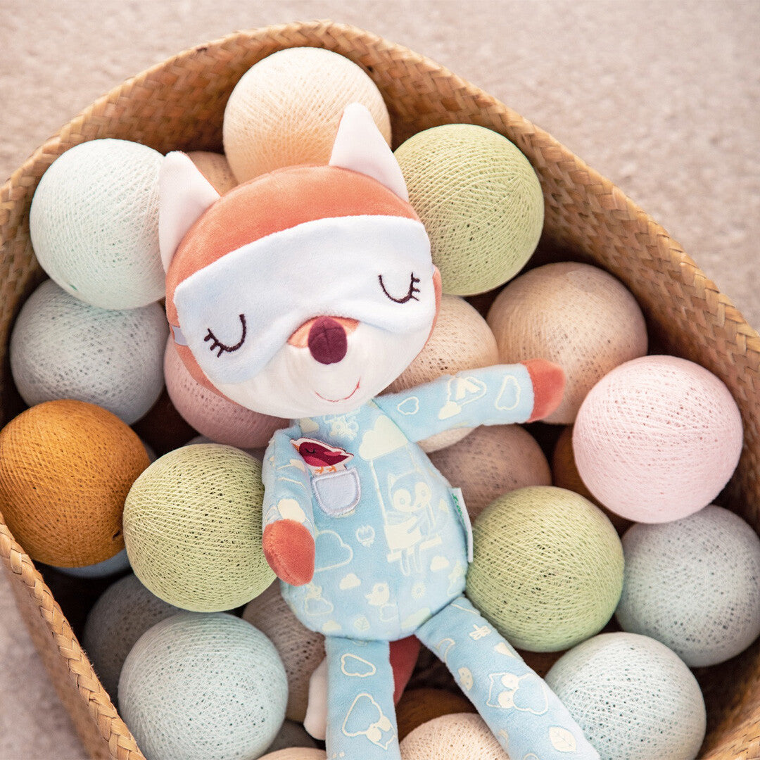 Lilliputiens pluchen slaapvriendje vos Alice ligt in een rieten mand gevuld met gekleurde bollen.