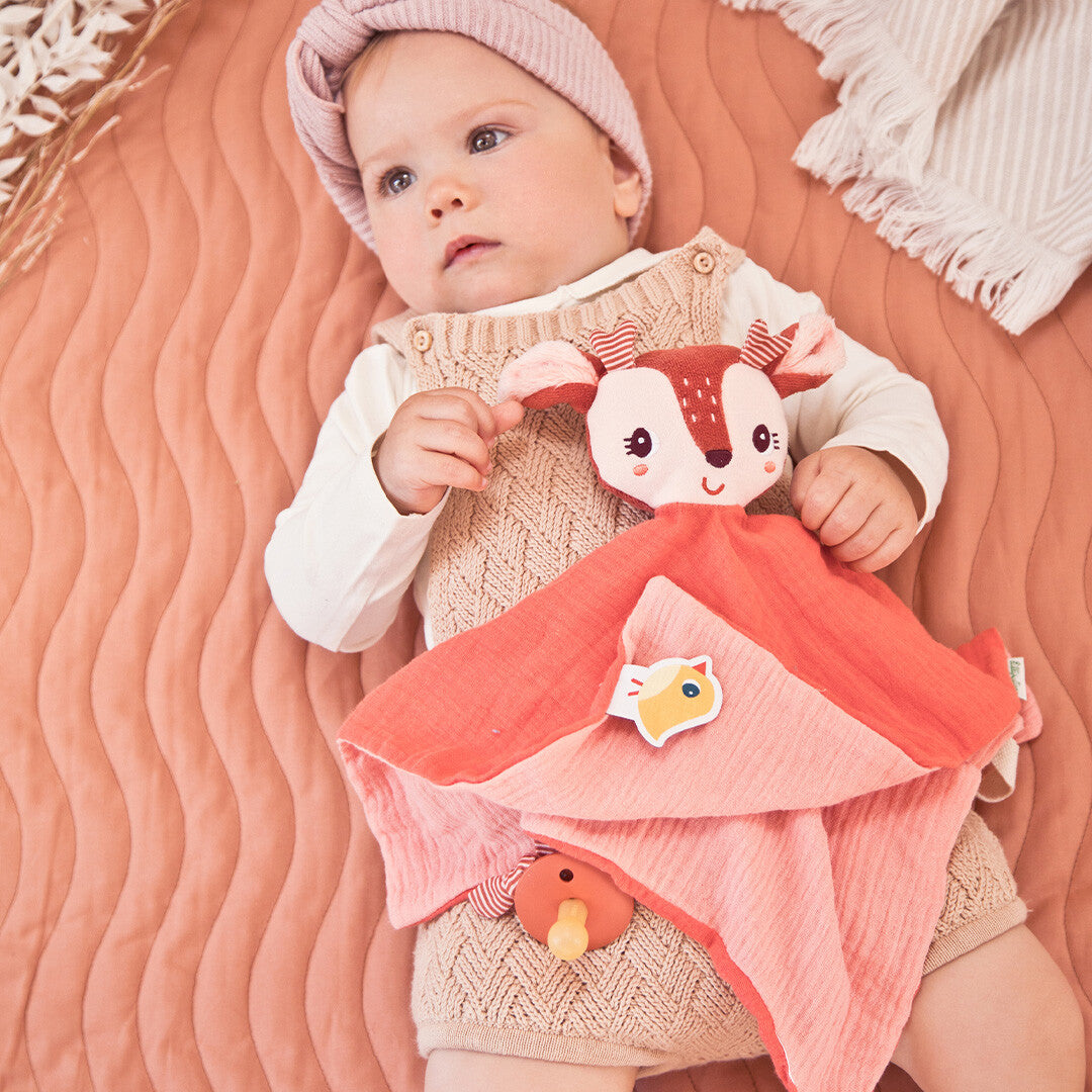 Baby ligt met Lilliputiens knuffeldoek Stella het hertje op een roze deken.