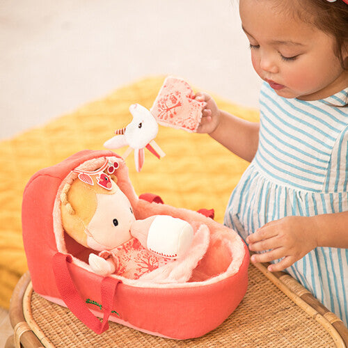 Een kindje speelt met de Lilliputiens lappenpop baby Lena in haar draagmand op een rieten krukje.