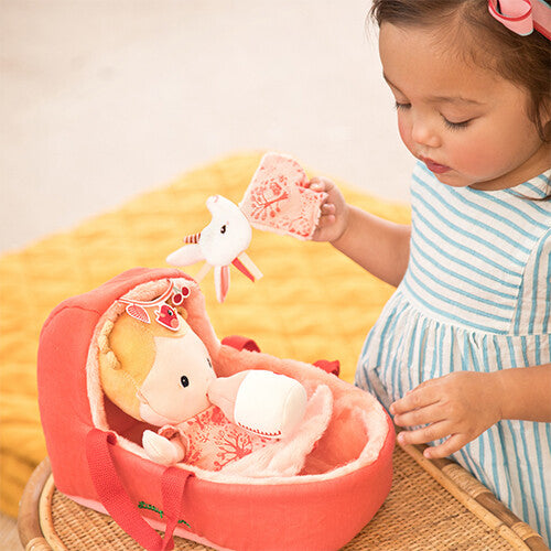 Een kindje speelt met de Lilliputiens lappenpop baby Lena in haar draagmand op een rieten krukje.