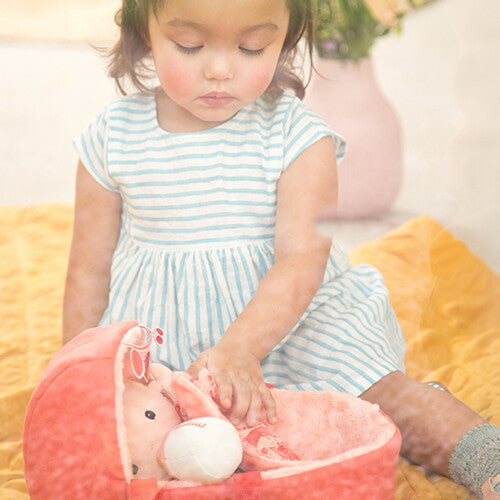 Een kindje speelt met de Lilliputiens lappenpop baby Lena in haar draagmand op een gele deken.