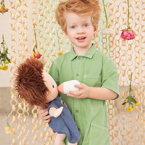 Een jongen met rood haar geeft de Lilliputiens lappenpop Charlie met blauwe romper een flesje.