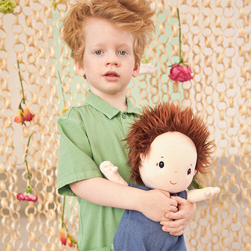 Een jongen met rood haar knuffelt de Lilliputiens lappenpop Charlie met blauwe romper.