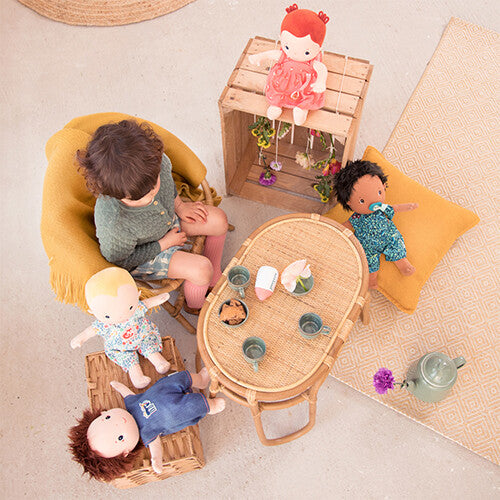 Een kind speelt met meerdere Lilliputiens lappenpoppen en een theeservies aan een rieten tafeltje.