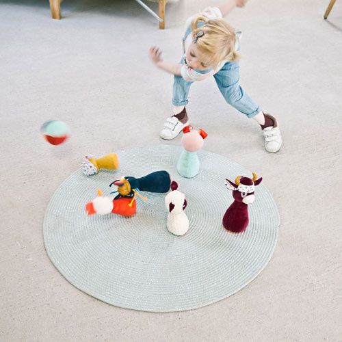 Een kind speelt met het Lilliputiens boerderijdieren kegelspel op een ronde mat.