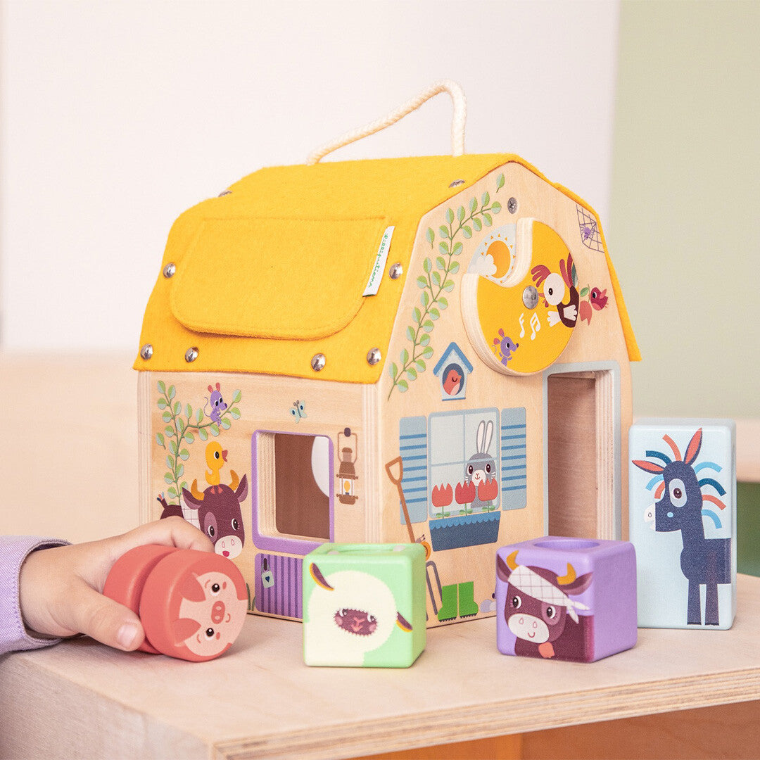 Een kinderhand speelt met het Lilliputiens houten ontdekkingshuis en de bijbehorende dierenvormen op een houten tafel.