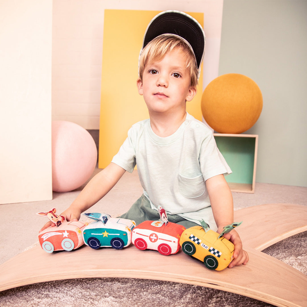Een jongen speelt met vier Lilliputiens stoffen pull-back speelgoedauto's, waaronder de gele taxi.