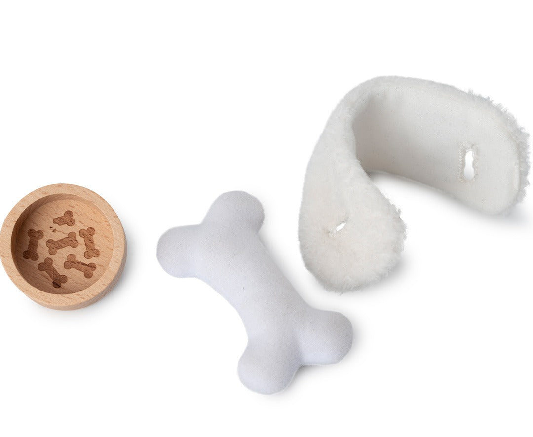 Detailfoto van de houten voerbak met botjes, een wit pluchen bot en een witte pluchen deken.