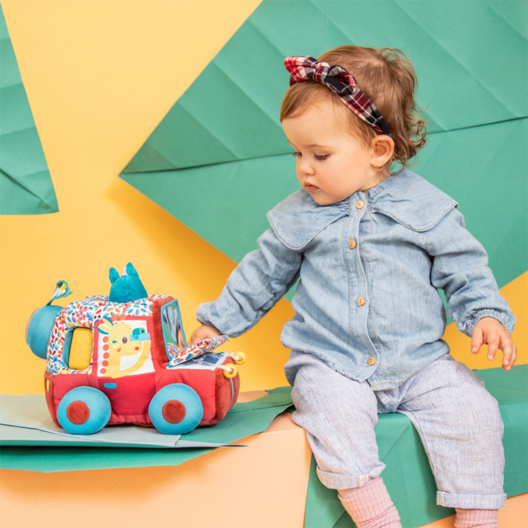 Een baby zit op een groene ondergrond en reikt naar de Lilliputiens activiteitenauto met safarithema.
