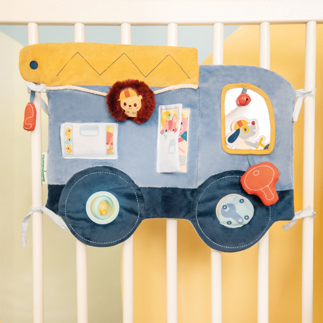 Het Lilliputiens activiteitenpaneel Jules de klusjesman hangt aan de spijlen van een wit babybedje.