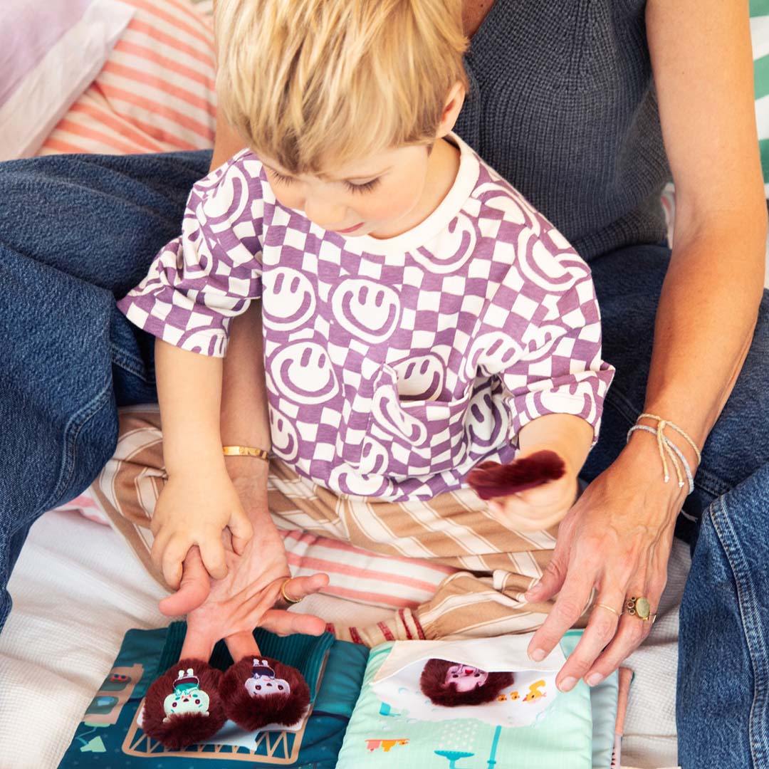 Een kind speelt met het Lilliputiens activiteitenboek en een egelpoppetje op schoot bij een volwassene.