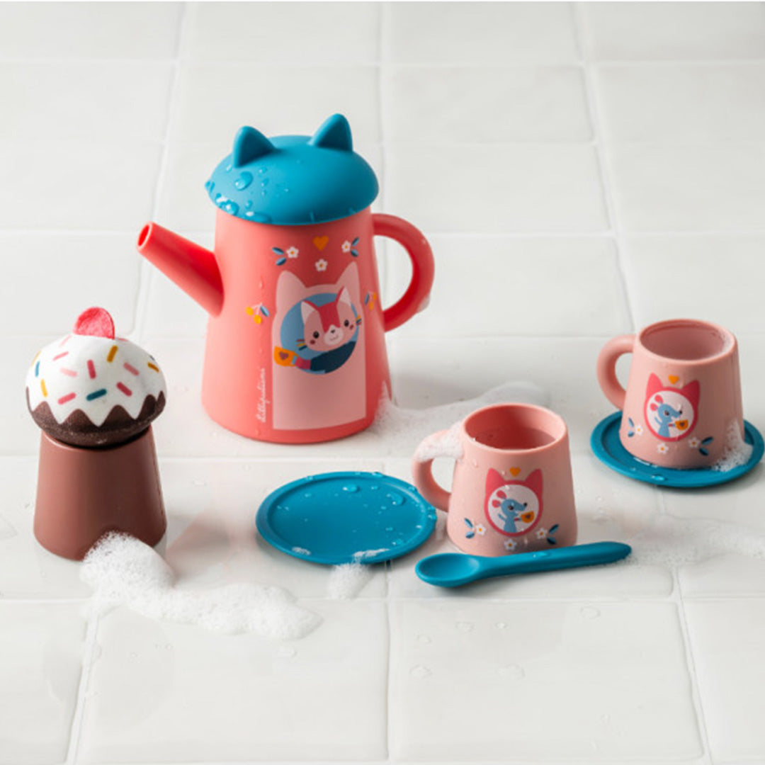 De Lilliputiens badspeelgoed theeset met roze theepot, twee kopjes, lepeltje en cupcake, met schuim op een witte tegelvloer.