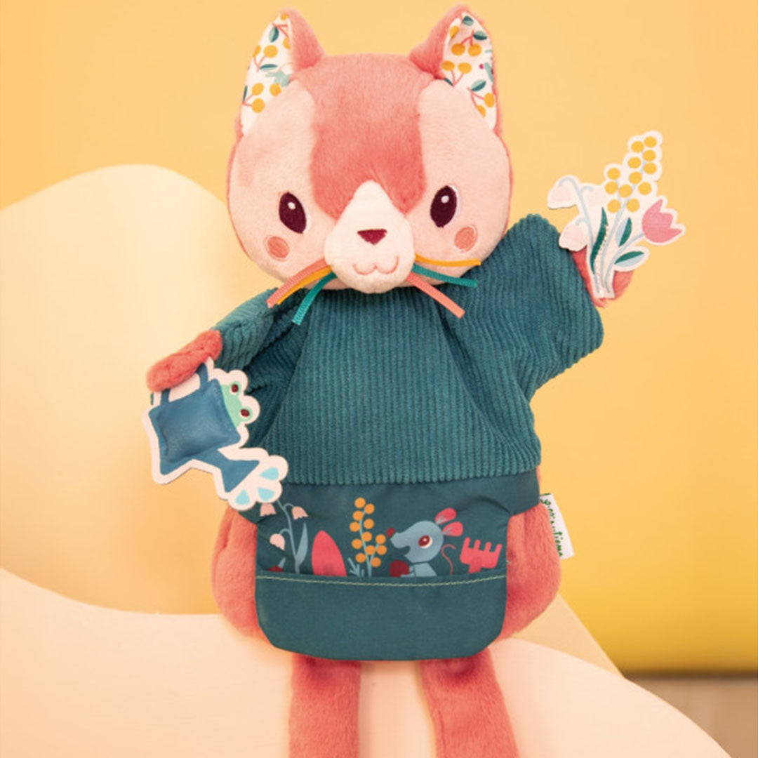 Lilliputiens handpop Jeanne, een roze kat met een gieter en bloemen, op een gele achtergrond.