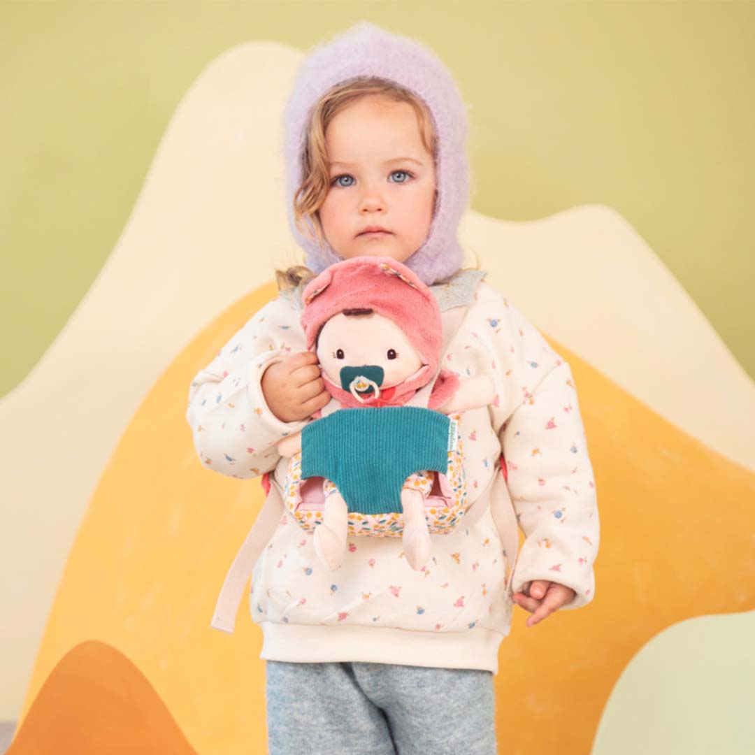 Een kind draagt de Lilliputiens lappenpop Jeanne in de gebloemde draagzak.