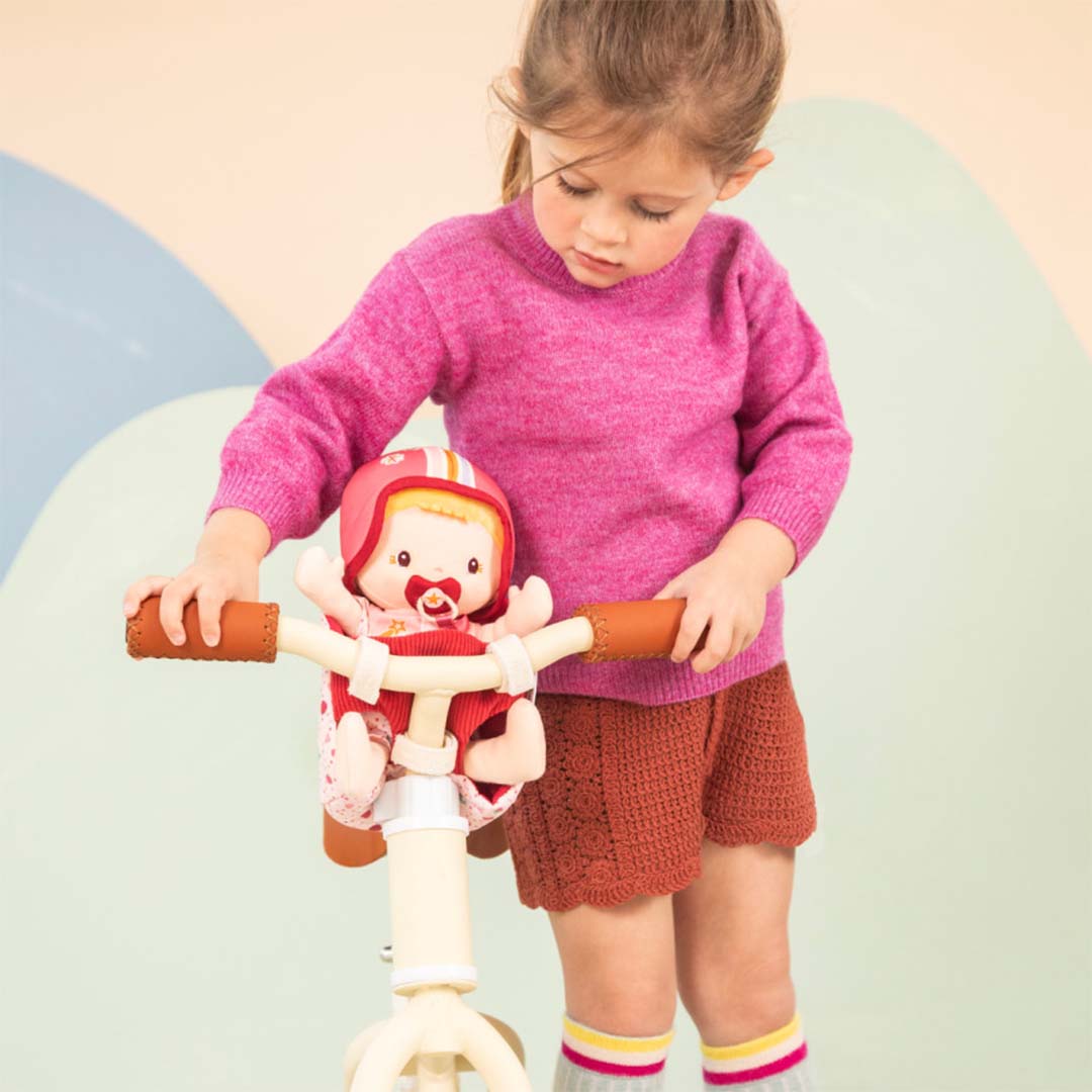 Een meisje kijkt naar de Lilliputiens lappenpop Lena in het roze fietszitje op een loopfiets.
