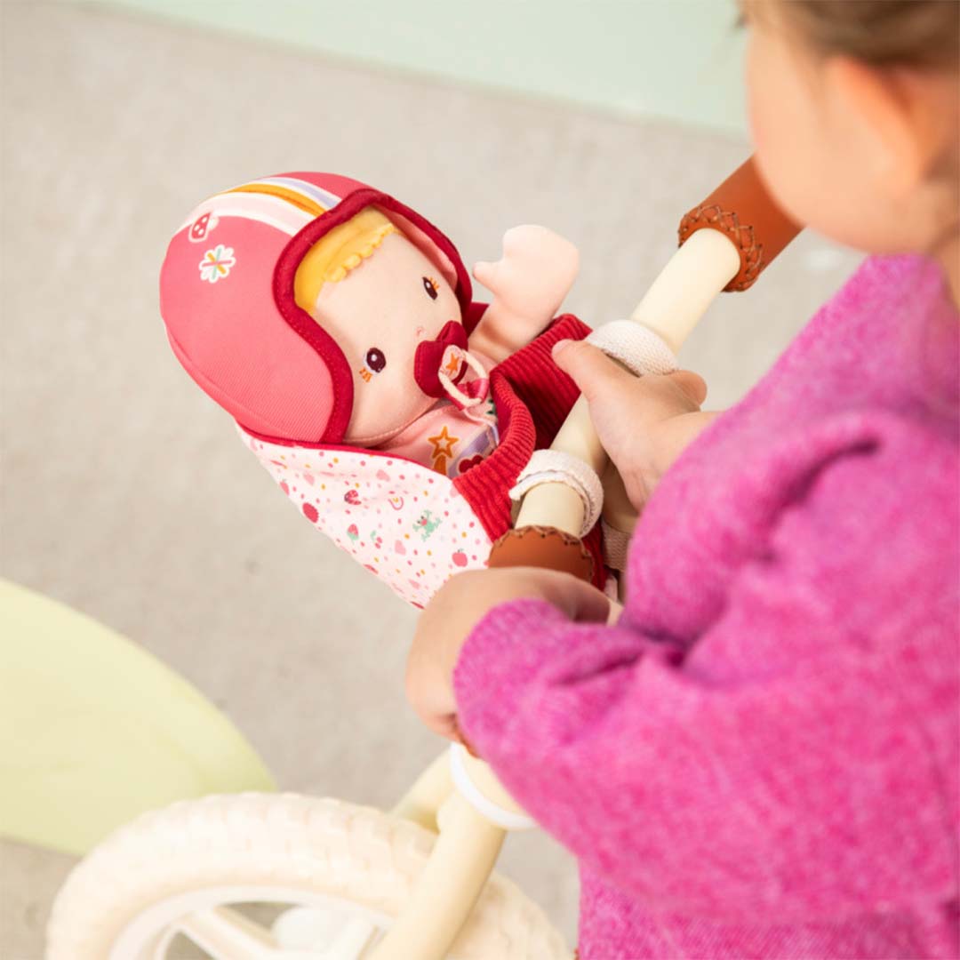 Close-up van een meisje dat speelt met de Lilliputiens lappenpop Lena in het roze fietszitje op een loopfiets.