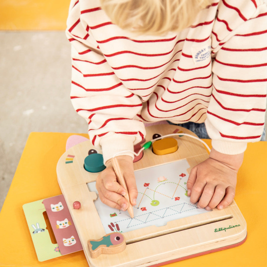 Kinderhanden tekenen met een potlood op het Lilliputiens magisch tekenbord, waarbij een sjabloon wordt gebruikt.