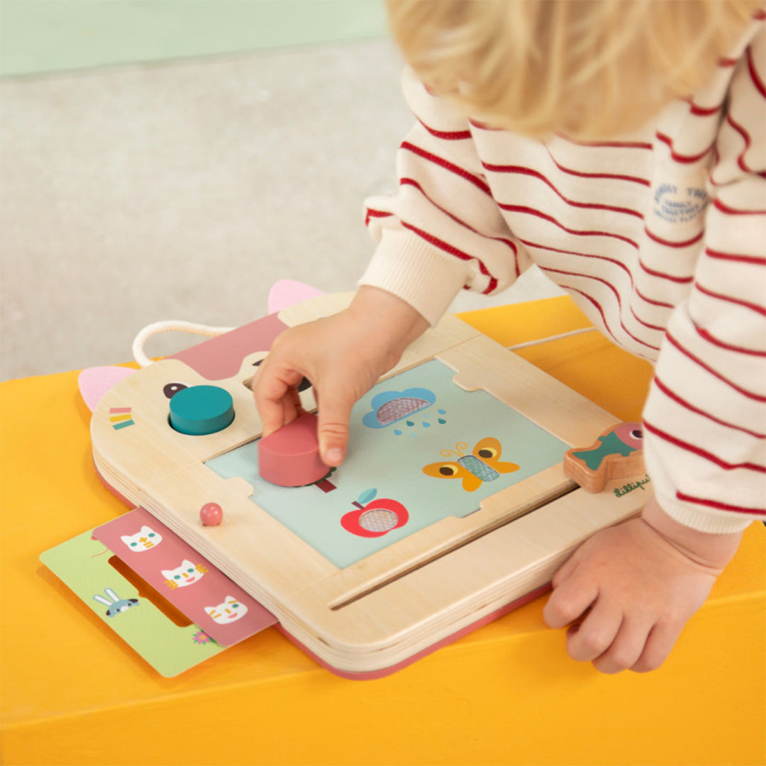 Kinderhanden plaatsen een sjabloon op het Lilliputiens magisch tekenbord, waarop een tekening van wolken en een vlinder te zien is.