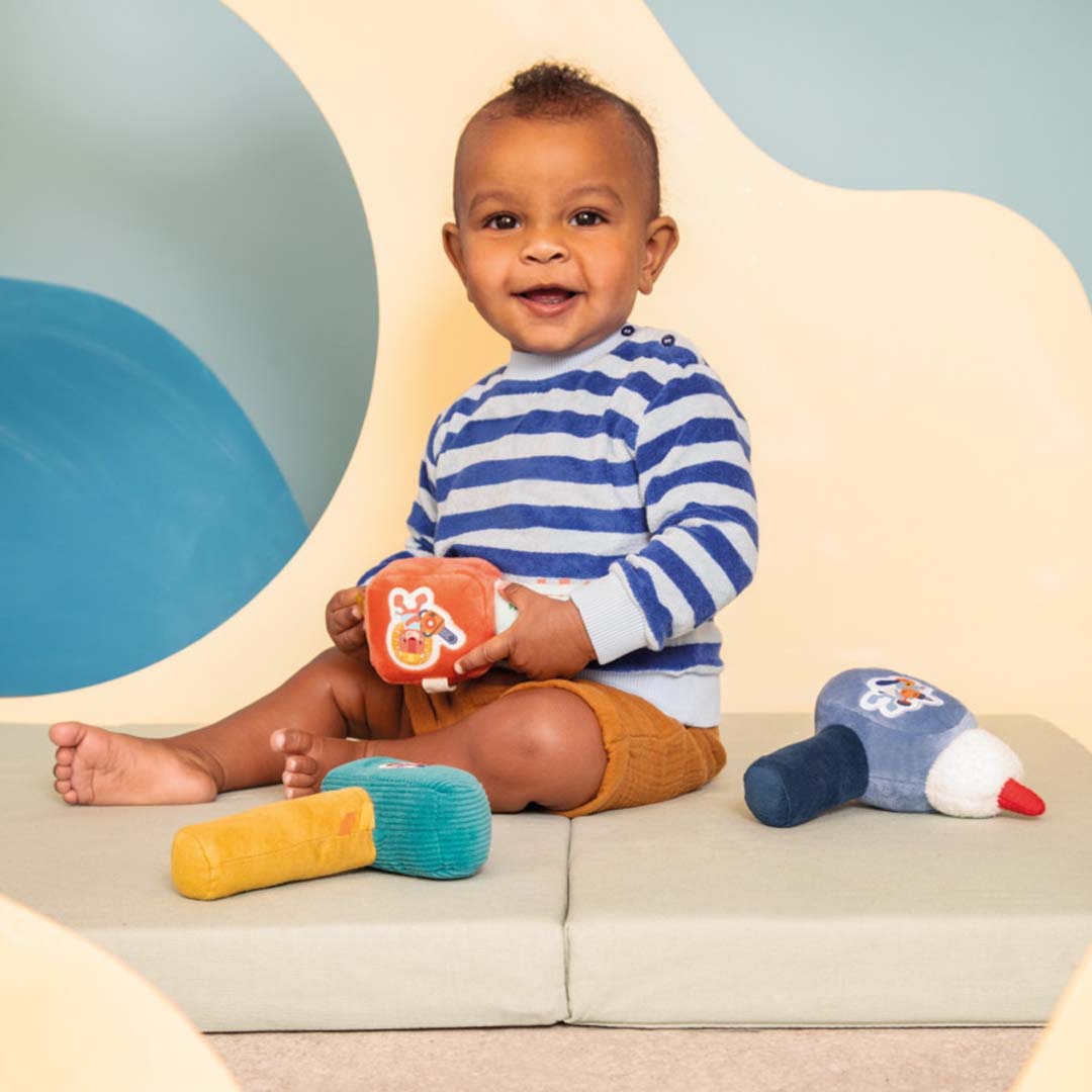 Een lachende baby speelt met de Lilliputiens kettingzaag rammelaar en andere zachte gereedschapsspeeltjes.