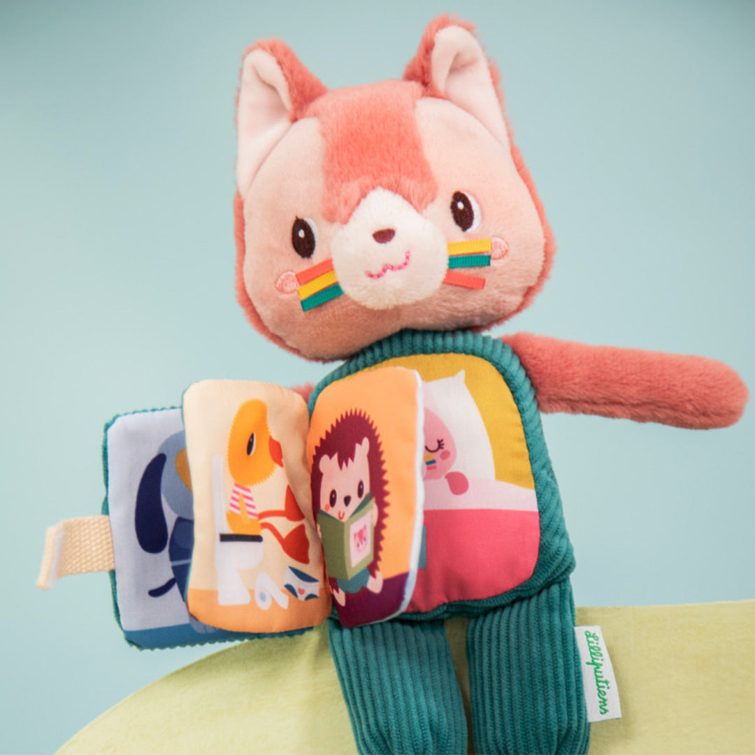 Lilliputiens vertelknuffel Jeanne zit met het huisje op haar buik opengeklapt, waar een zacht boekje met dierenillustraties zichtbaar is.