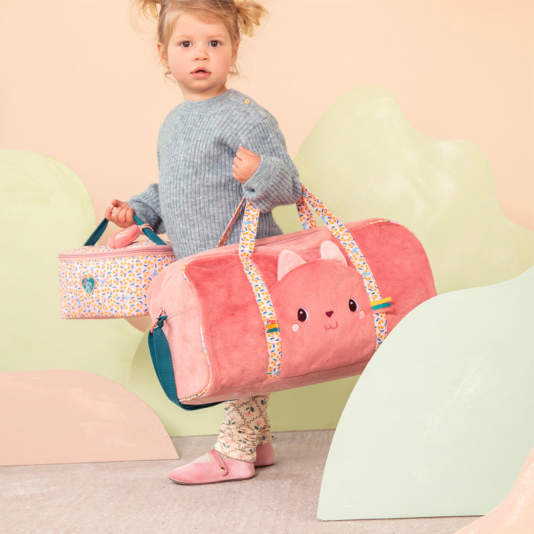 Een jong kind draagt de Lilliputiens roze kinderweekendtas met kattengezicht en een bijpassende toilettas.