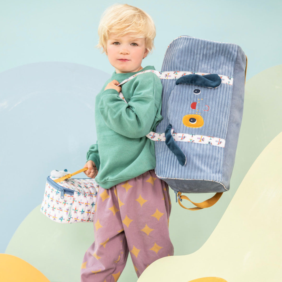 Een kind draagt de Lilliputiens weekendtas met hondenhoofd op de schouder en een bijpassende lunchtas in de hand.