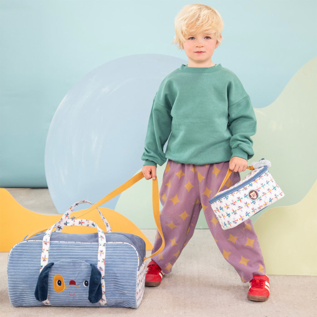 Een kind staat naast de Lilliputiens weekendtas met hondenhoofd en houdt een bijpassende lunchtas vast.