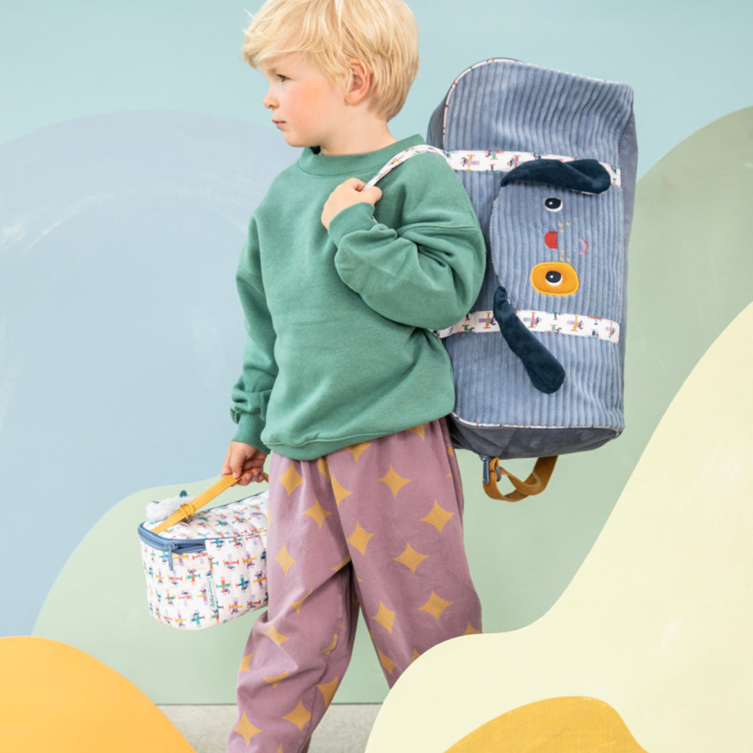 Een kind loopt met de Lilliputiens weekendtas met hondenhoofd op de schouder en een bijpassende lunchtas in de hand.