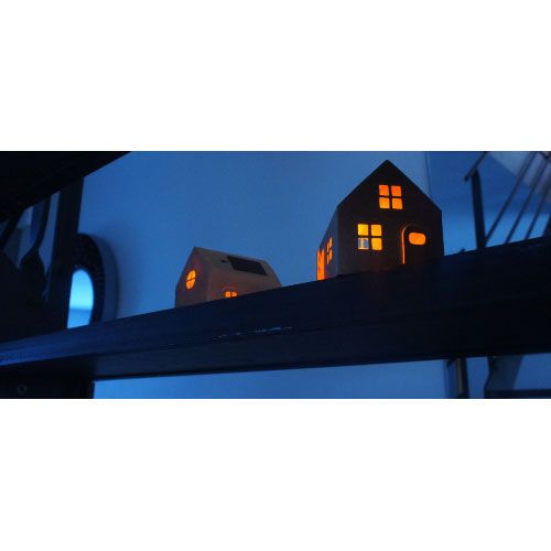 Twee verlichte bouwpakketje huisjes met zonnepaneel staan op een donkere plank.