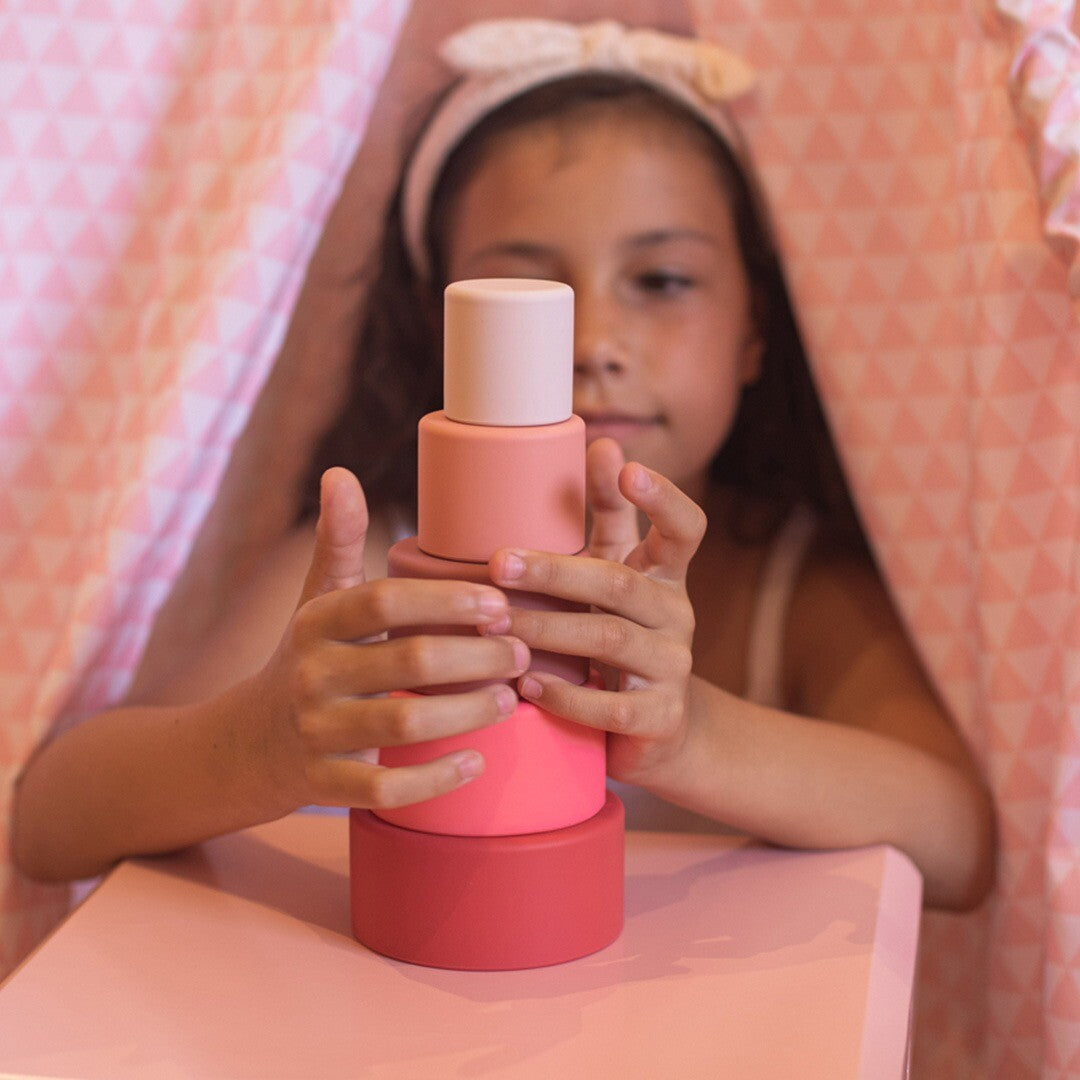Een meisje stapelt de little l rood-roze stapelkommen op elkaar in een roze tent.