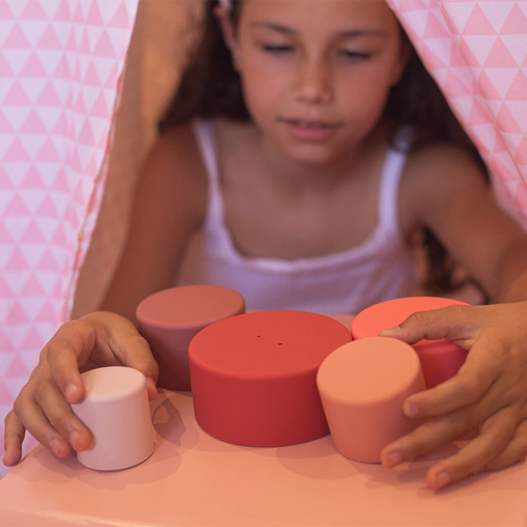 Een meisje speelt met de losse little l rood-roze stapelkommen op een roze tafel.