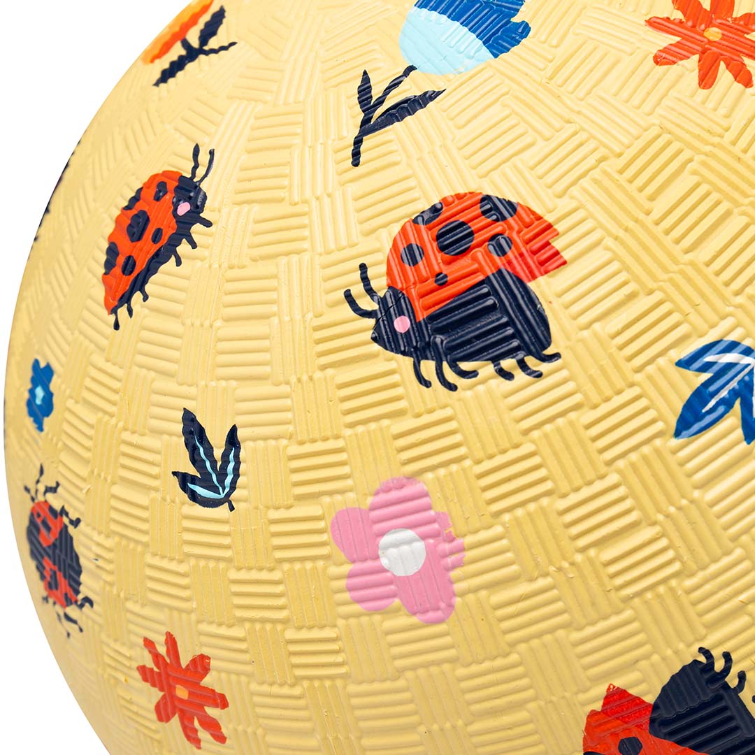 Detail van de little l speelbal met lieveheersbeestjes en bloemen op een beige ondergrond.
