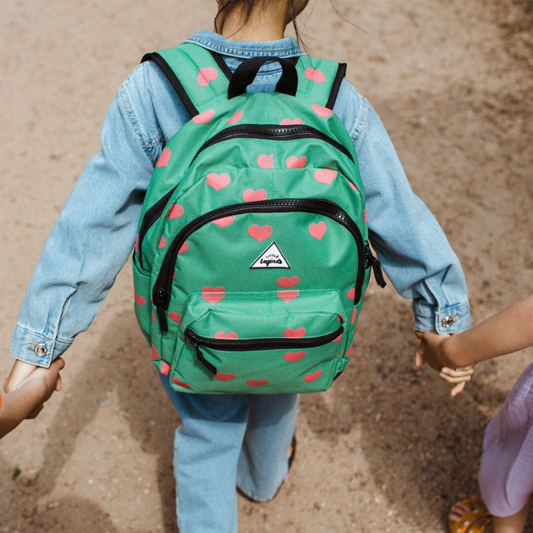 Kind draagt de little legends groene kinderrugzak met roze harten op de rug, van achteren gezien.